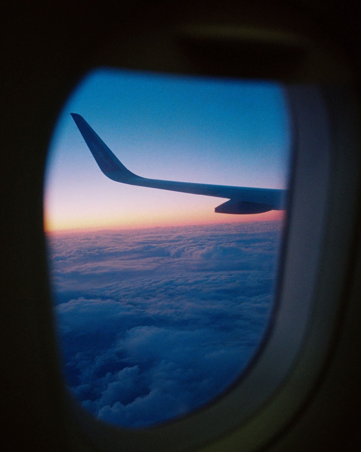 Private jet wing above the clouds at sunset, seen through a cabin window